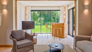 Een moderne woonkamer met een grote schuifpui naar een tuin, een flatscreen televisie, rieten meubels en een houten kast.