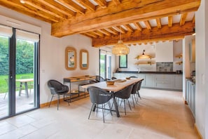 Une cuisine moderne avec un plafond en bois, un coin repas avec une table et des chaises, et une vue sur un jardin grâce à de grandes portes coulissantes.
