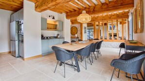 Een ruime keuken met een houten plafond, een grote eettafel met stoelen en een hangende lamp.