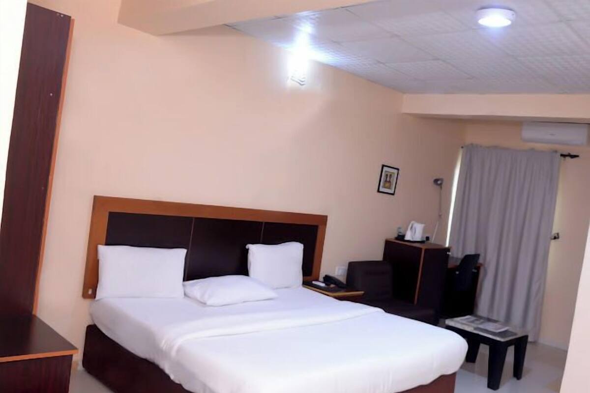 A hotel room with a large bed, a desk, a chair, and a window with curtains.