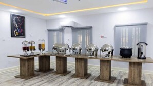A dining area with a long wooden table, multiple serving stations, and a modern ceiling design. - Bliss World Resorts & Hotels (Akure)