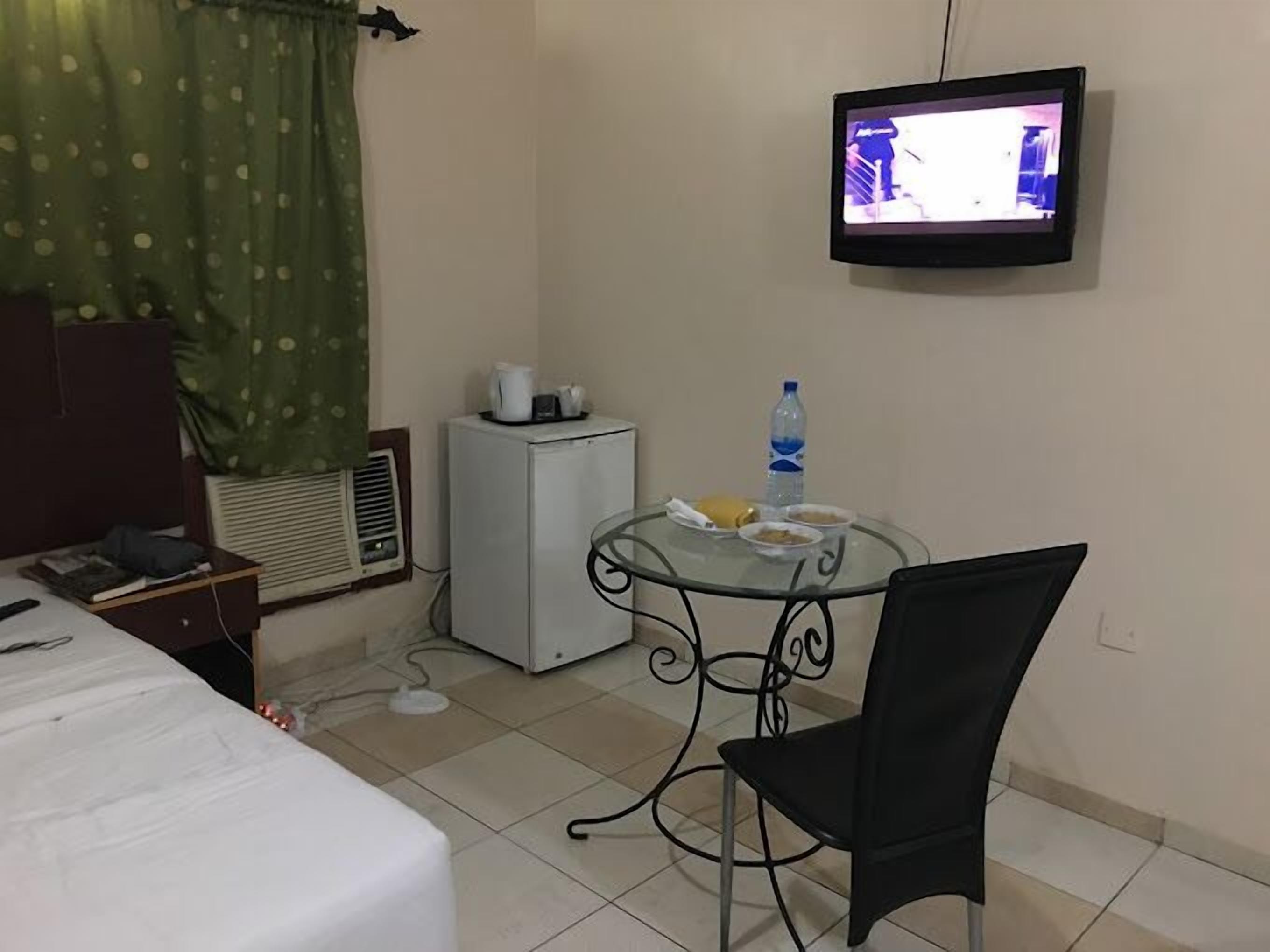 A hotel room with a bed, a small table with a chair, a television mounted on the wall, a mini-fridge, and a window with curtains.