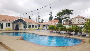 A swimming pool with tiled flooring, surrounded by outdoor seating and a building with a tiled roof. - Bliss World Resorts & Hotels (Akure)