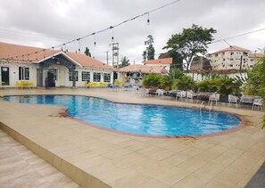 A swimming pool with tiled flooring, surrounded by outdoor seating and a building with a tiled roof. - Bliss World Resorts & Hotels (Akure)