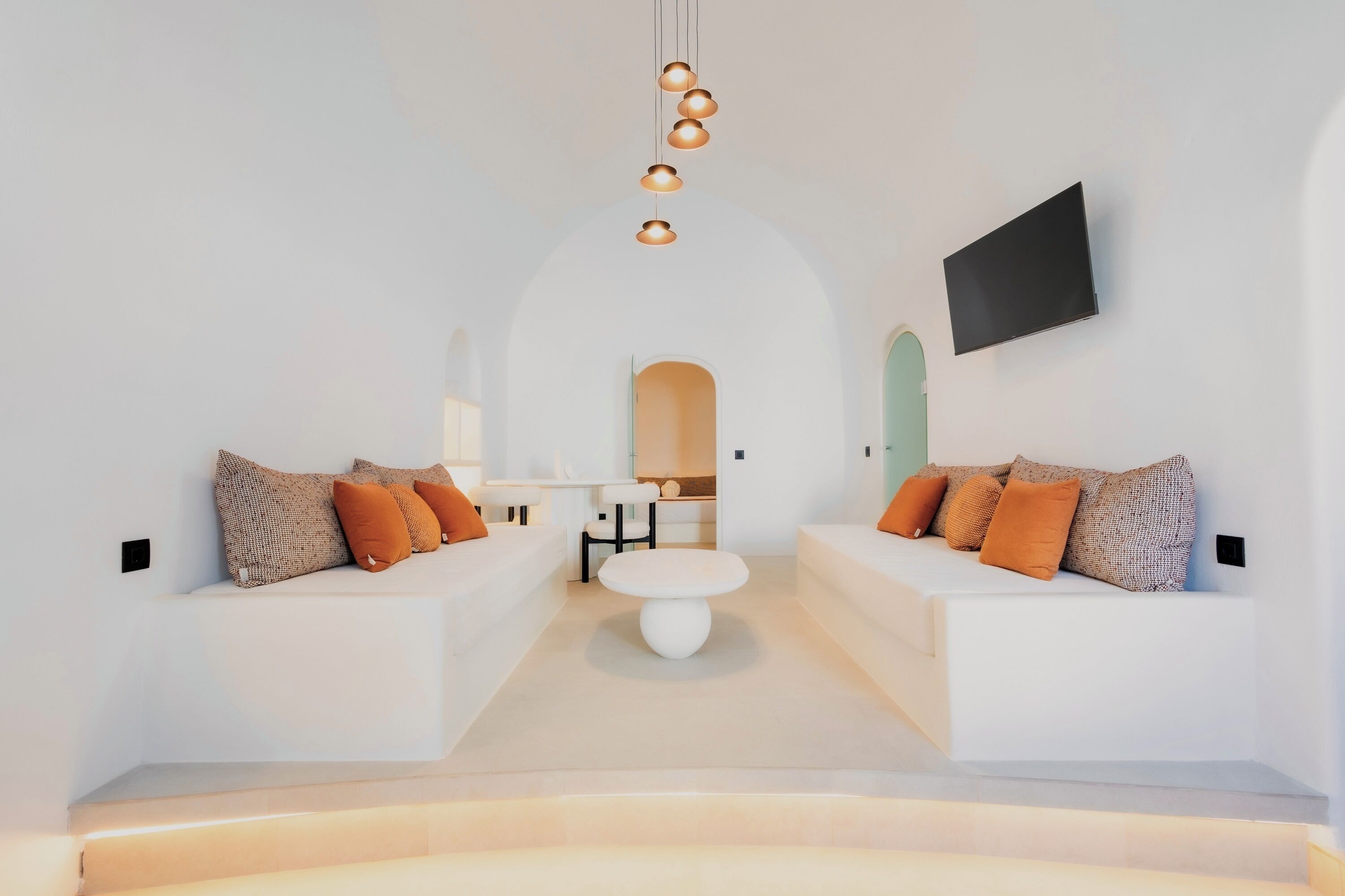 Et moderne interiør med hvide sofaer, et rundt spisebord i midten og et fjernsyn ophængt på væggen.
