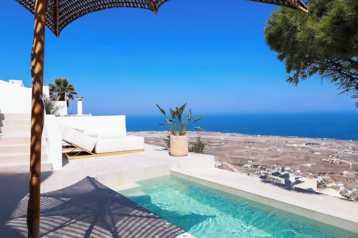 A pool area with a view of the sea, white outdoor furniture, and a potted plant.