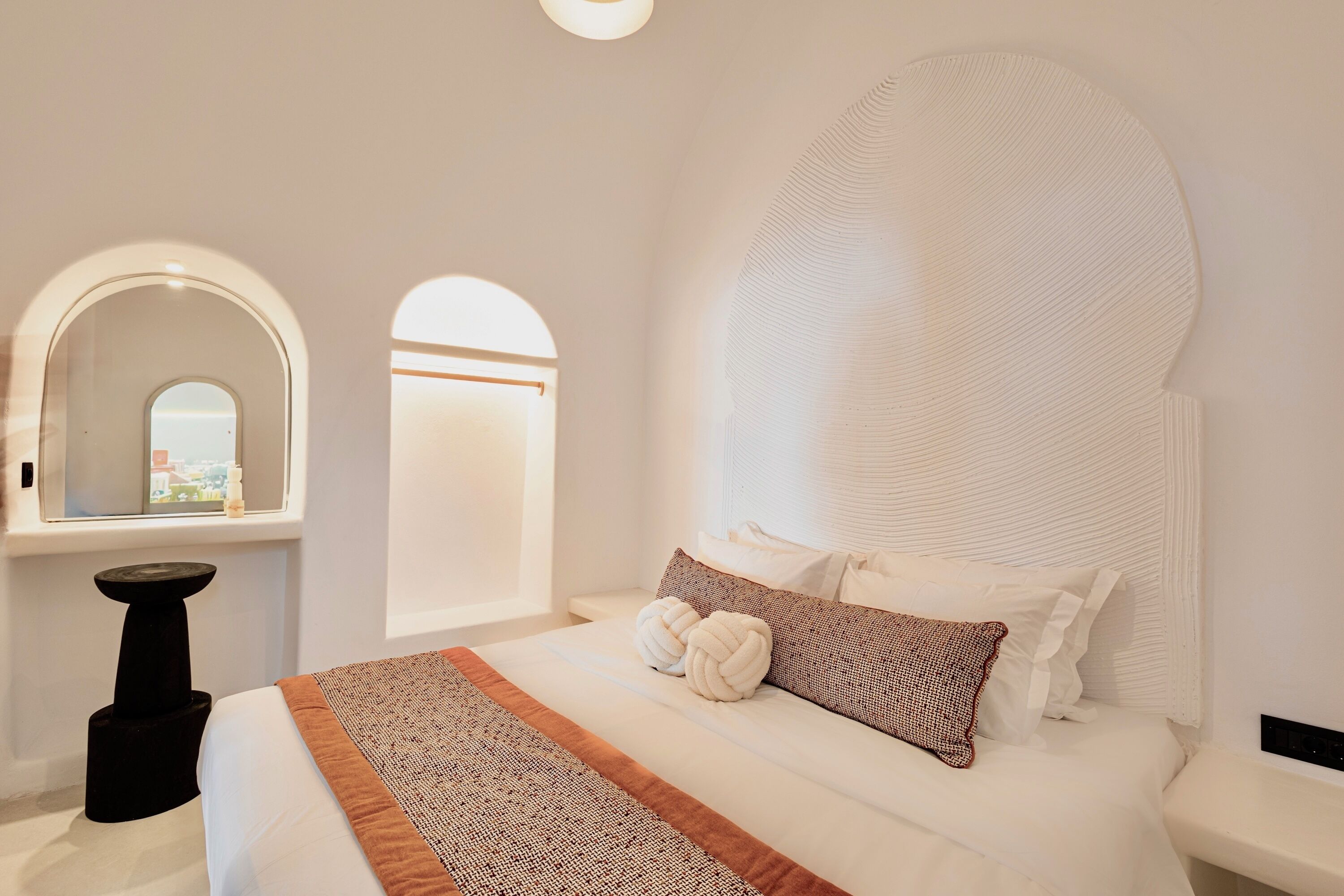 Una habitación de hotel moderna con una cama grande, cabecera redonda y vistas a través de un ventanal en arco.