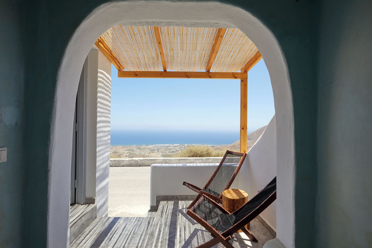 A view from a covered outdoor area with a wooden bench and a chair, overlooking a coastal landscape.