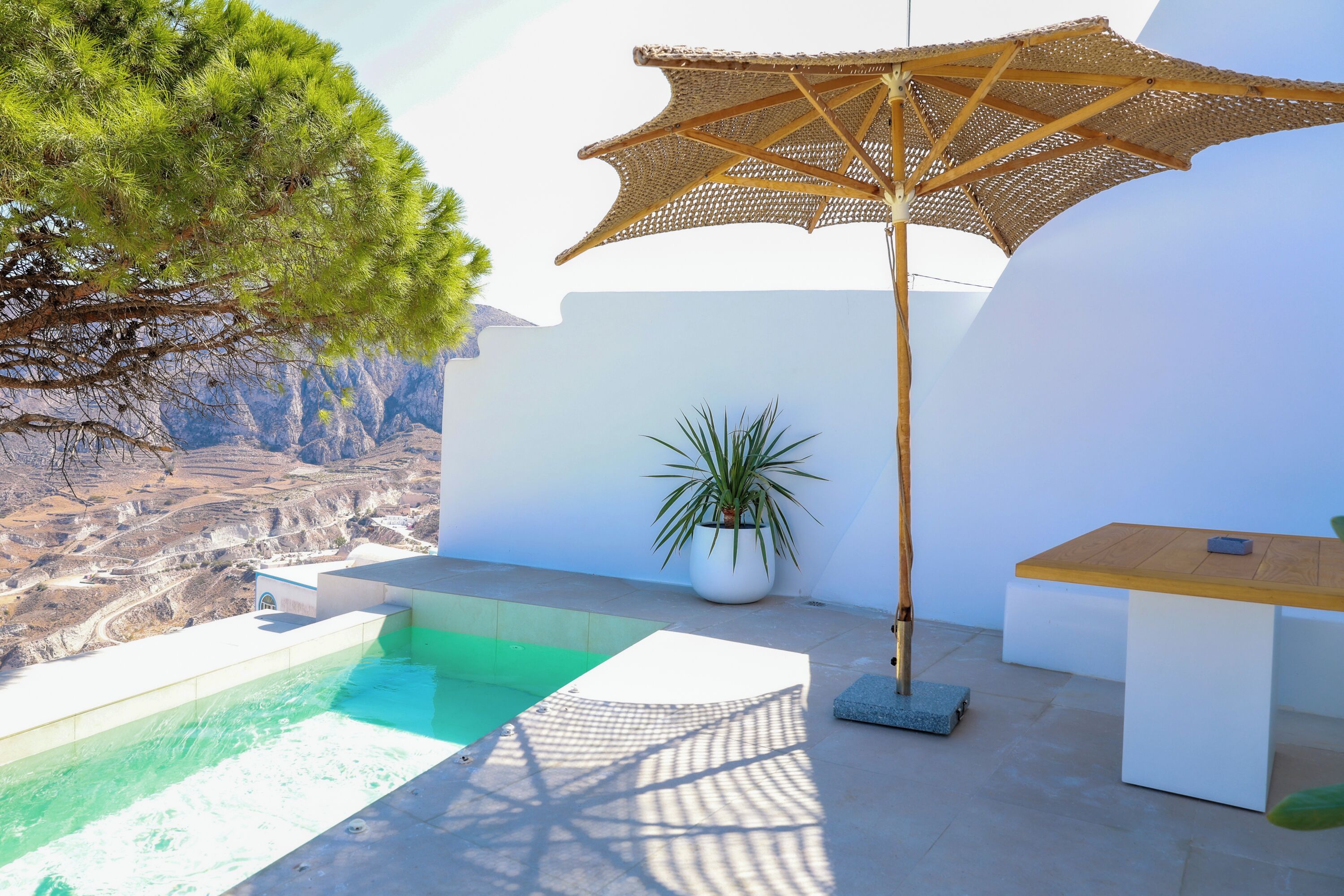 Un espace aménagé au bord de la piscine, avec une table en bois, un parasol en fibres naturelles et une plante en pot.