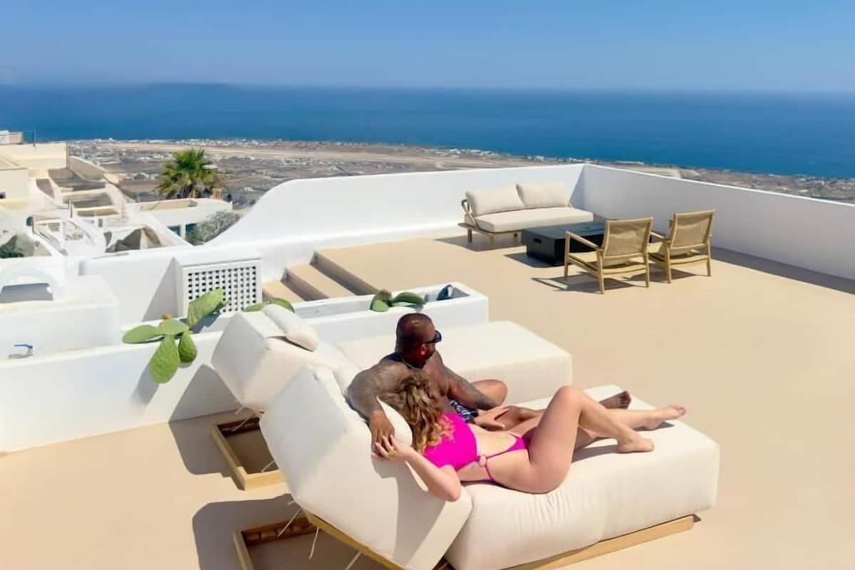 A rooftop terrace with white lounge chairs, a pool, and a view of the sea.