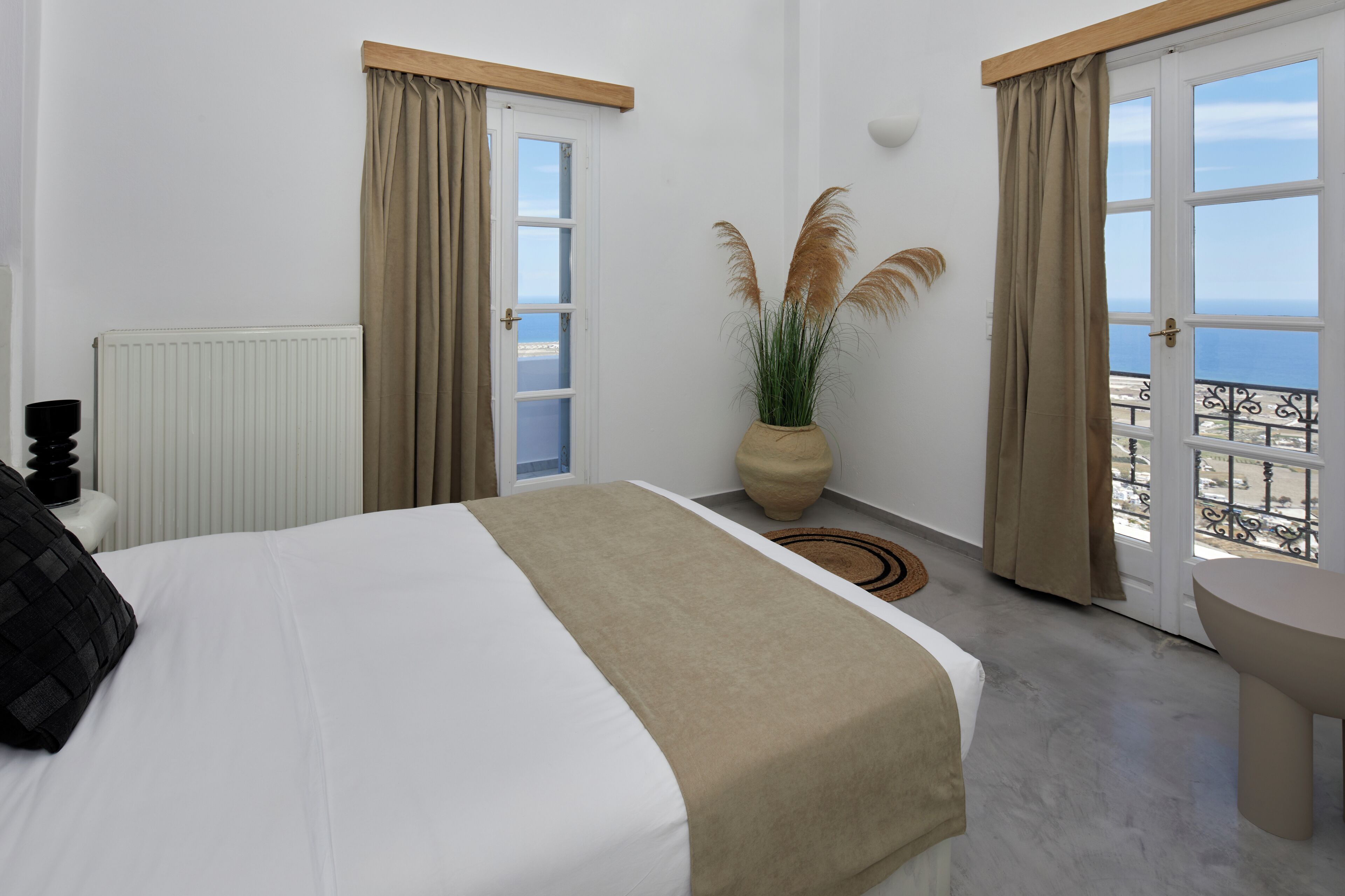 Una camera d'albergo con un letto, una pianta in vaso, vista sul mare e un balcone con ringhiera.