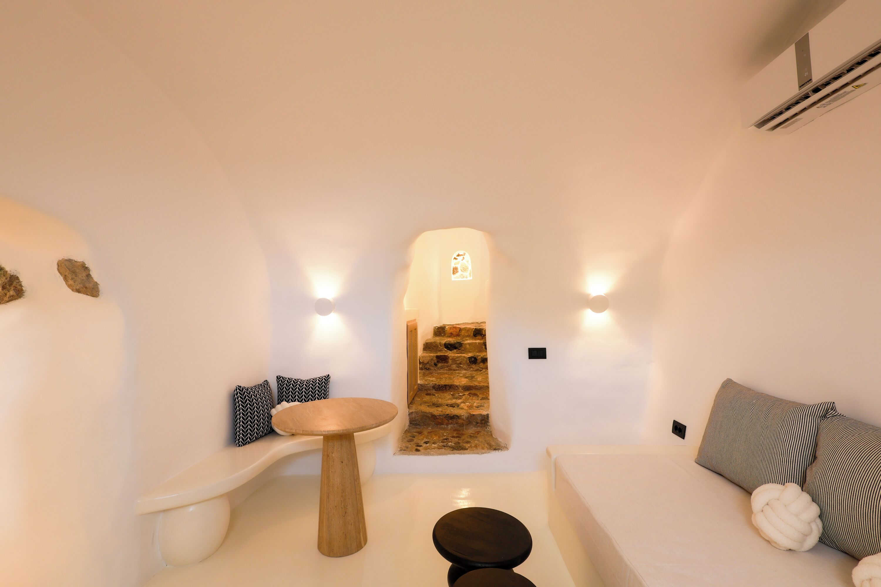 Una habitación moderna y minimalista con paleta de colores blanca, una mesa de madera, un sofá con cojines y una pared de piedra.
