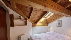 Un dormitorio con techo inclinado, vigas de madera, una cama, un radiador y una estantería con un objeto decorativo.