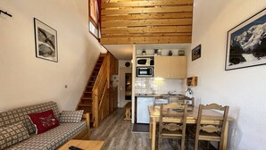 Un espacio habitable compacto con una escalera de madera, kitchenette, comedor y sofá.