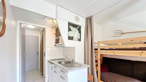 A compact kitchen with a sink, microwave, and cabinets, adjacent to a bunk bed with a curtain. - Bright Studio 4 pers, Ski-in/Ski-out, Pets allowed (Le Corbier)