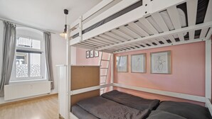 Une chambre avec un lit superposé, une fenêtre, un radiateur et une œuvre d’art encadrée au mur.