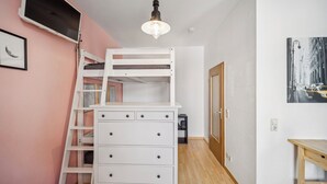 Une chambre avec un lit superposé, une commode, un téléviseur, un luminaire et une porte.