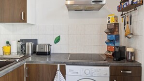 Une cuisine moderne équipée d’un lave-linge intégré, d’une hotte en acier inoxydable, ainsi que de divers appareils de cuisine et ustensiles disposés sur le plan de travail.