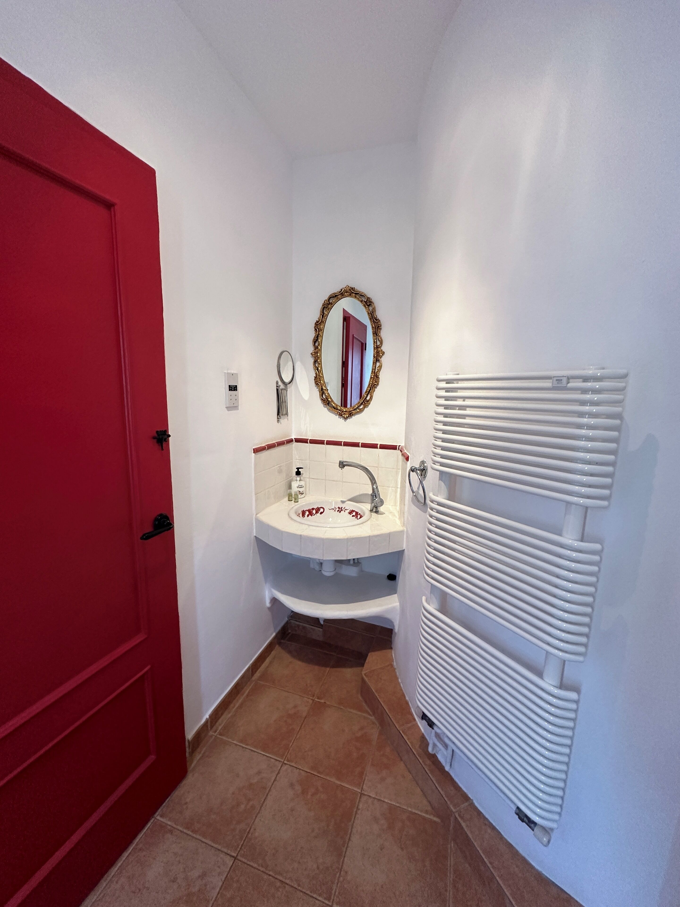 A bathroom with a red door, a white sink with a mirror above it, and a white radiator.