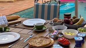 A dining table set with plates, cutlery, a loaf of bread, a bowl of fruit, and a bottle of juice. - Casa del Patio PdV (El Pinar)