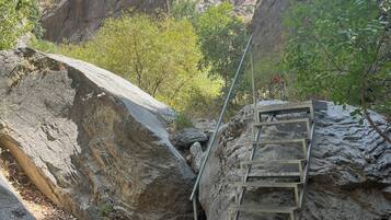 Terreno rocoso con una escalera metálica que asciende por una pendiente pronunciada, rodeado de grandes rocas y vegetación escasa.