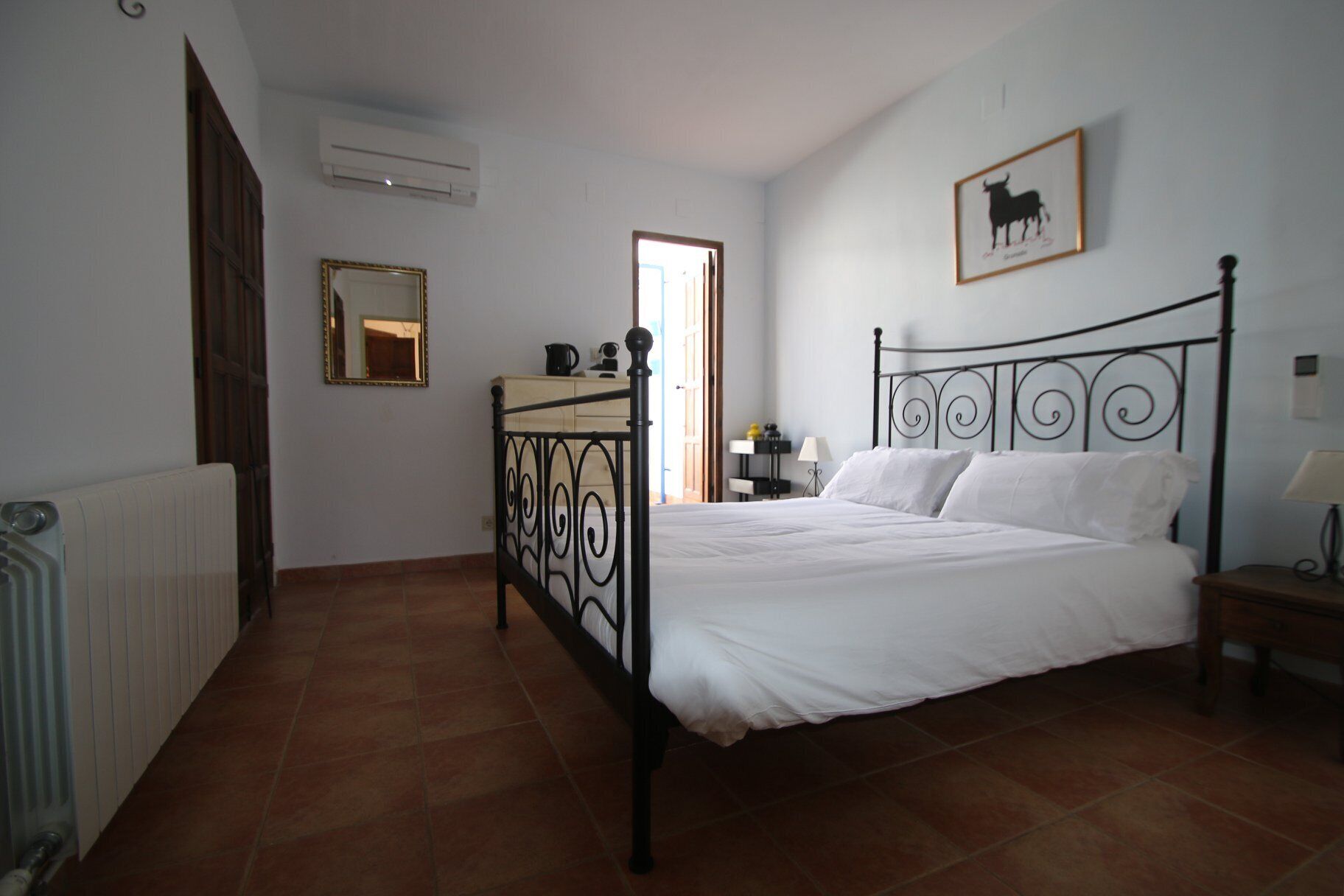 Une chambre à coucher comprenant un lit, une table de chevet, un miroir, un radiateur et une porte.