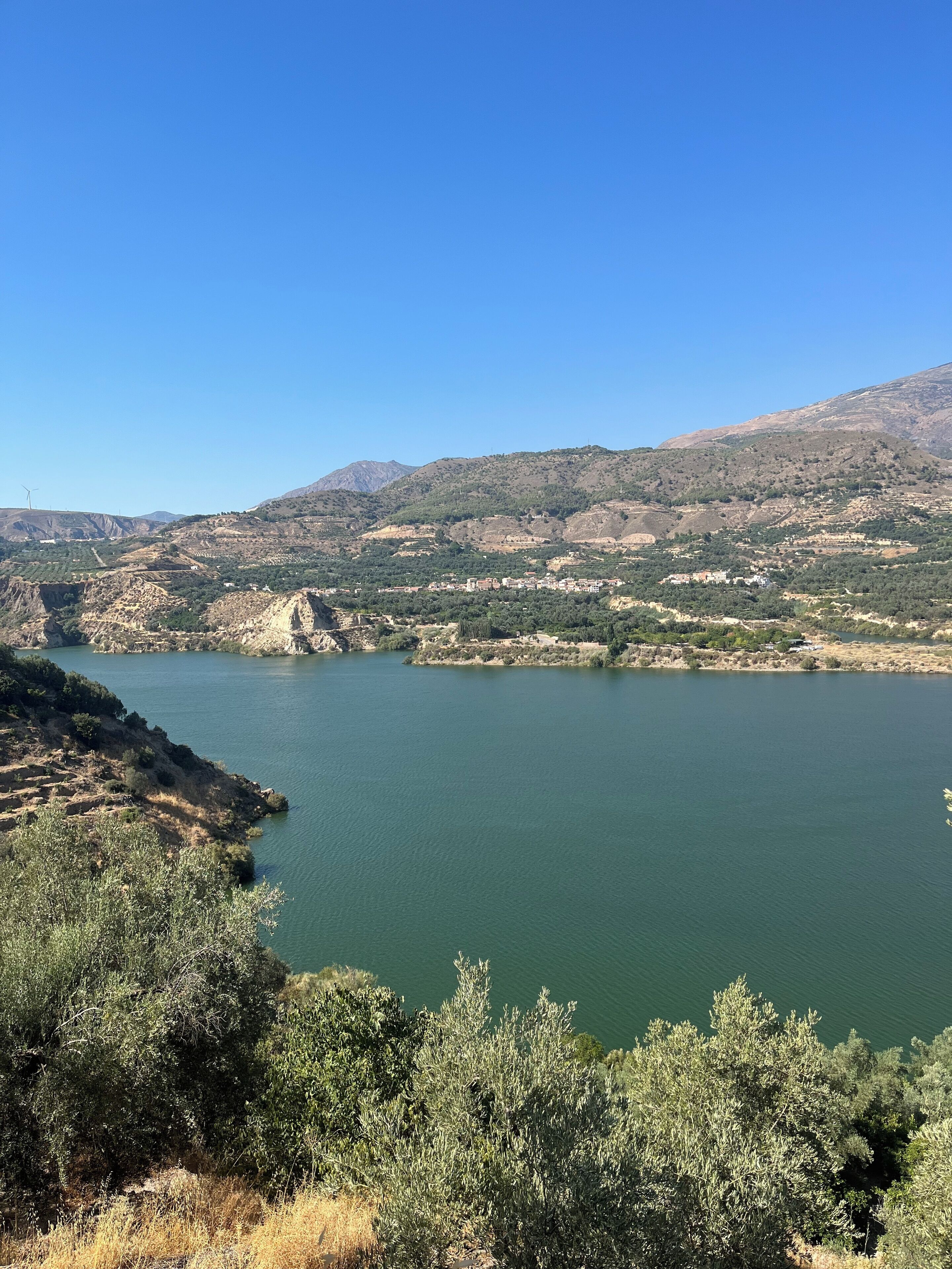 A panoramic view of a lake surrounded by hills and sparse vegetation.