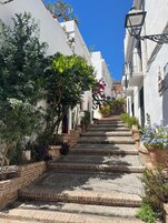 Una calle estrecha con edificios blancos, una escalera y plantas en macetas.