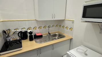 Uma cozinha compacta com armários brancos, uma pia, um micro-ondas e uma geladeira pequena.