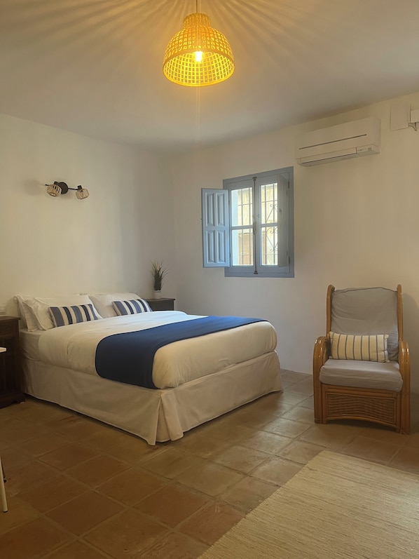 Un dormitorio con cama, una silla, un ventanal y una lámpara colgante.