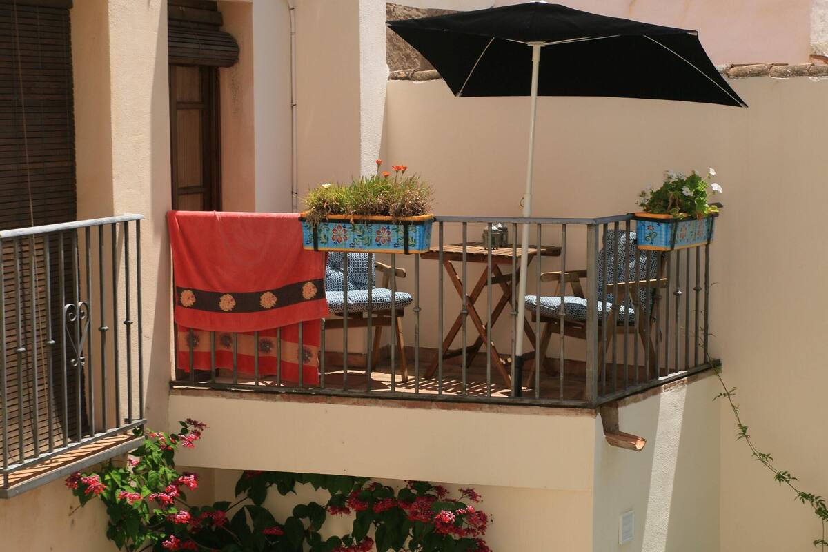 A balcony with a black umbrella, two chairs, a table, and potted plants.