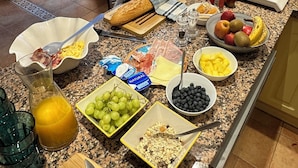 A kitchen counter with breakfast items, including eggs, bread, fruits, and a cutting board with a tomato. - Casa del Patio PdV (El Pinar)