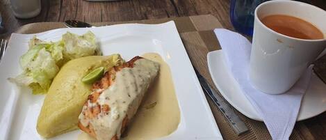 A plate with a fish fillet, a side of lettuce, and a cup of coffee on a table.