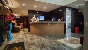 Een hotel receptie met een marmeren vloer, een receptiebalie en een televisiescherm.