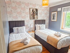 A hotel room with two beds, a nightstand, a lamp, a framed picture, and a window with a view. - Dingle Town Holiday Home (Dingle)
