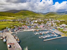A coastal town with a marina, houses, and green hills in the background.