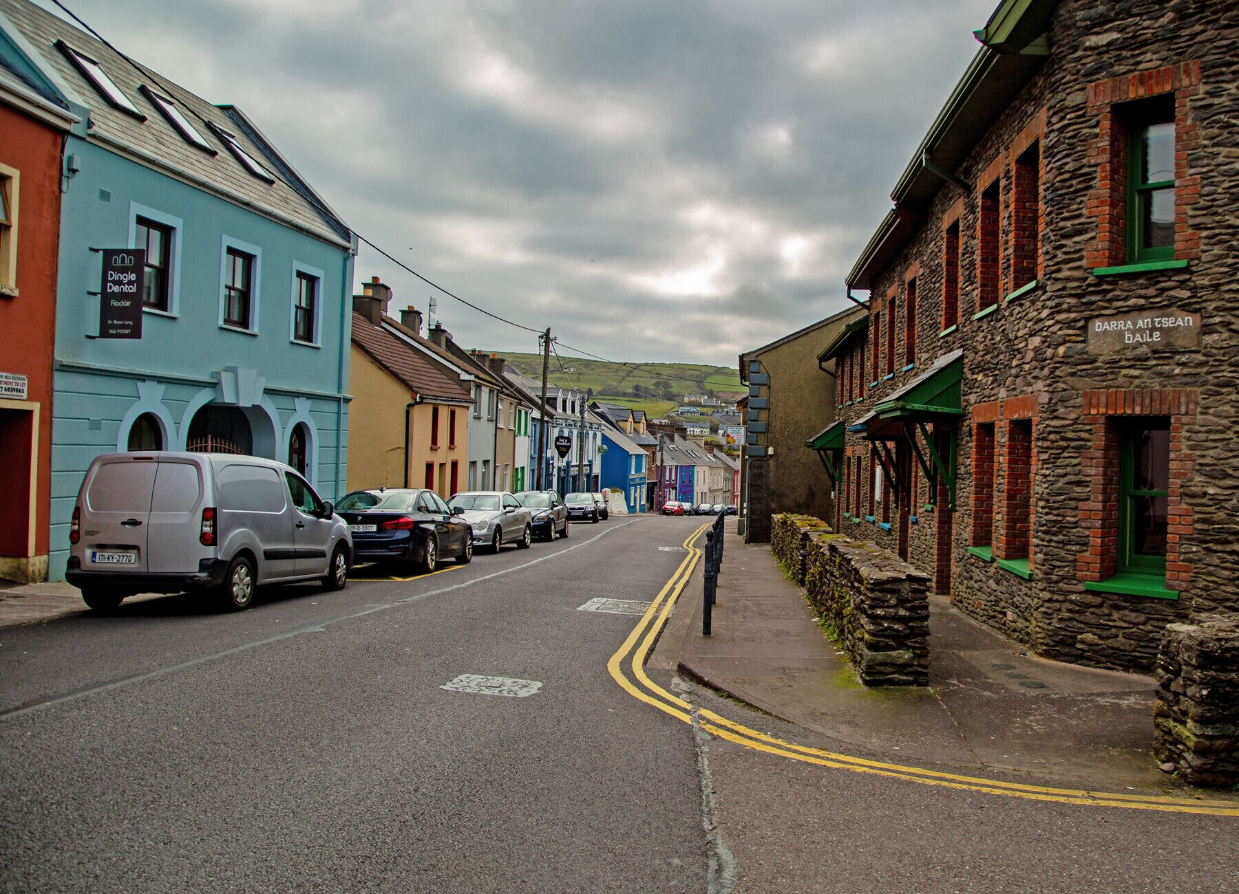 A narrow street lined with colorful buildings, including a dental clinic and a stone building with a sign.