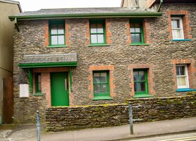 A stone building with green windows and doors, a stone foundation, and a small porch area.