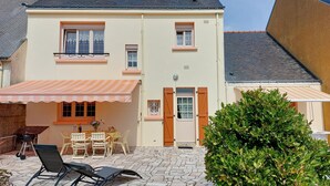 Una casa de dos pisos con un patio, mobiliario exterior y un pequeño jardín.