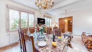 Un comedor con una mesa de mármol, sillas ornamentadas, una araña y un televisor al fondo.