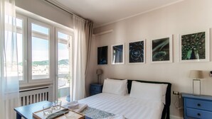 A hotel room with a bed, a desk with a tray, a nightstand, and a window with curtains. - Turchese (Como)