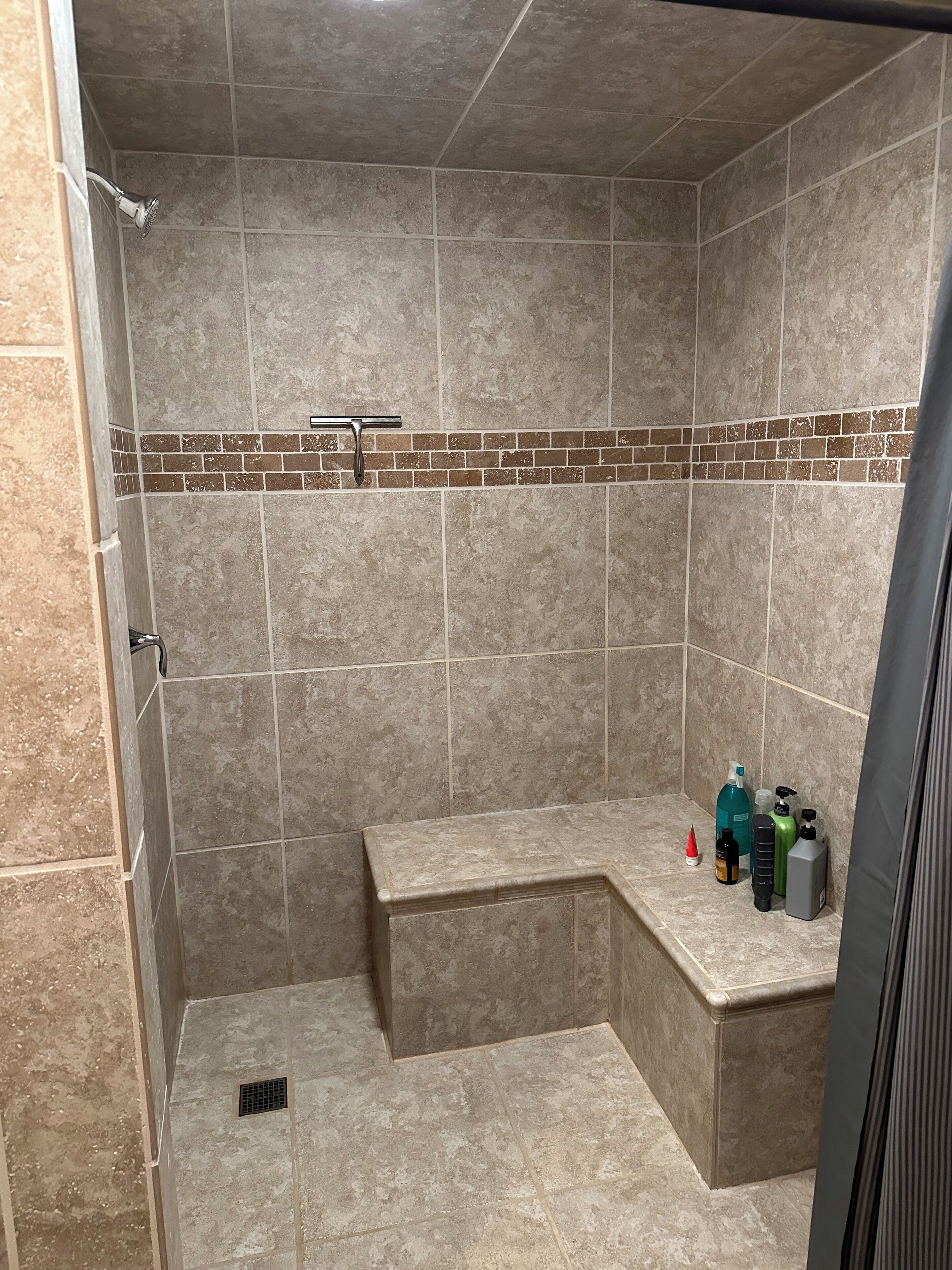 A shower area with beige tiles, a bench, and toiletries on a ledge.