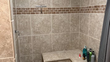 A shower area with beige tiles, a bench, and toiletries on a ledge.