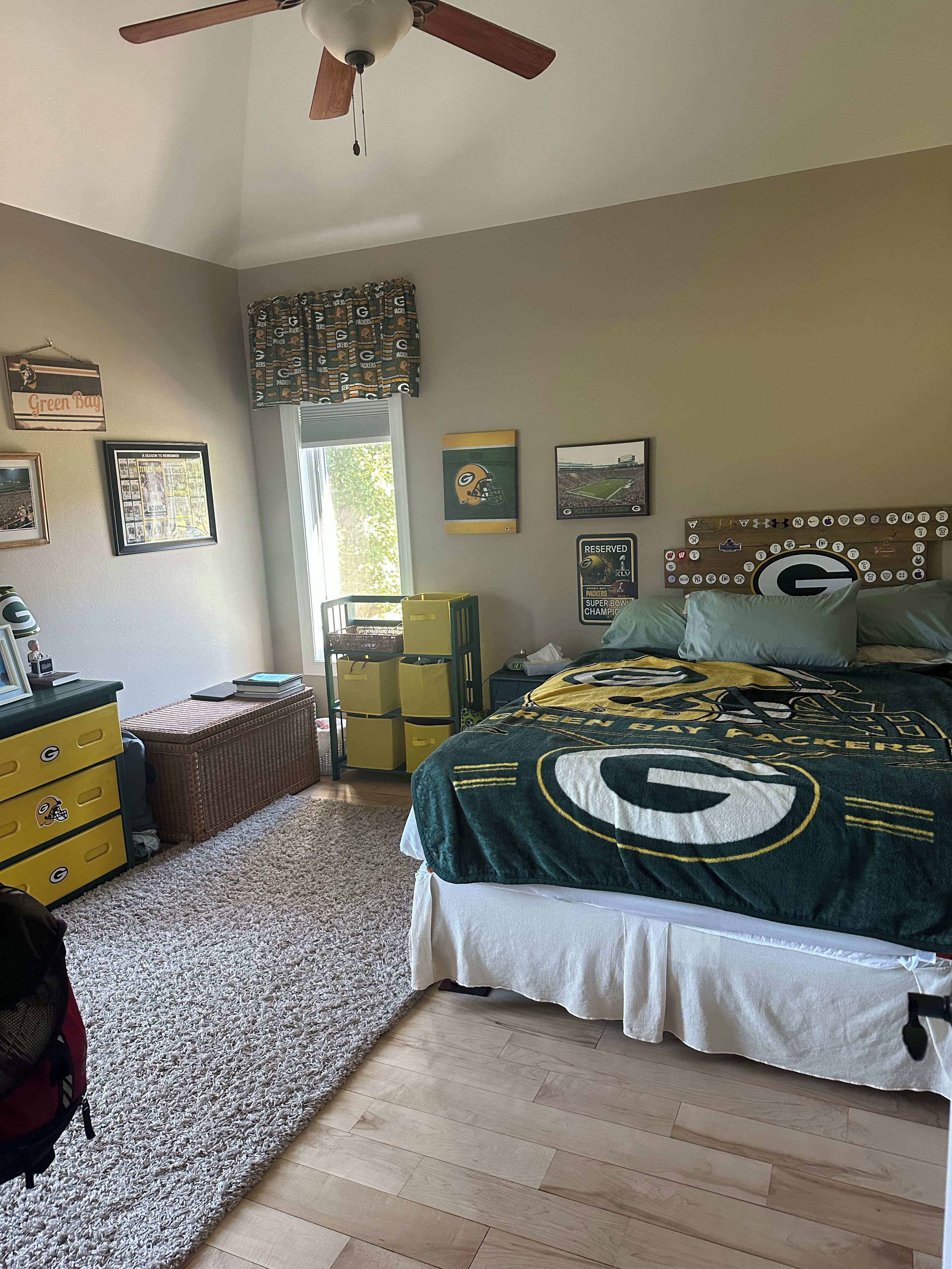 Une chambre à coucher avec un lit orné du logo d’une équipe de football, un ventilateur de plafond et une fenêtre avec des rideaux.