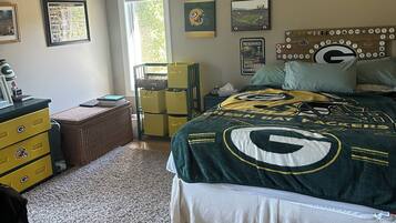 Une chambre à coucher avec un lit orné du logo d’une équipe de football, un ventilateur de plafond et une fenêtre avec des rideaux.