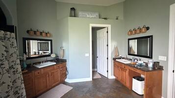 A bathroom with two sinks, wooden cabinets, a mirror, and a door leading to another room.