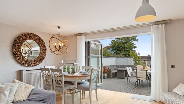 A modern living room with a dining area, a large mirror, and a view of the outdoor patio. - Ger Y Mor - Village Centre With Parking (Saundersfoot)