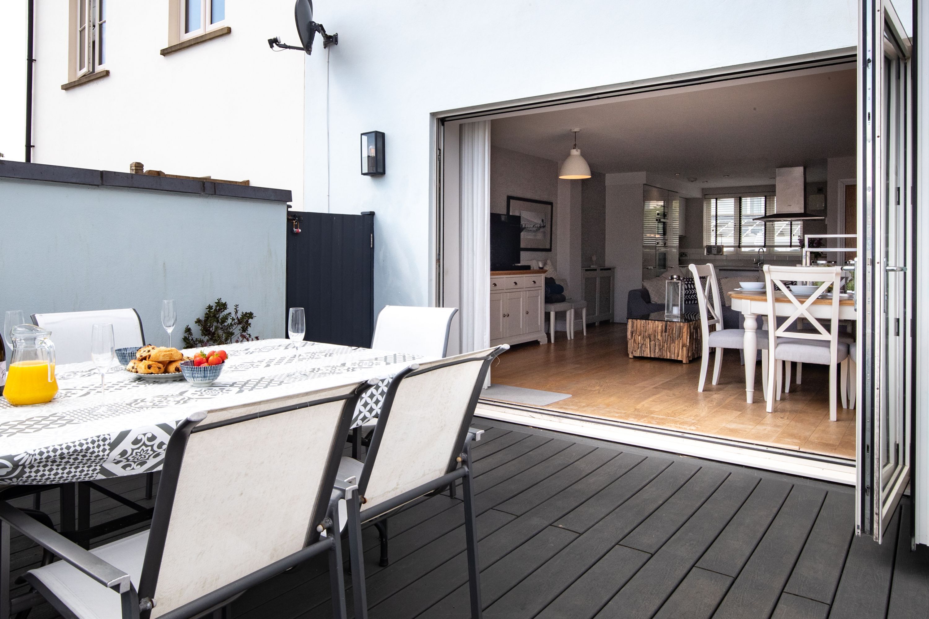 An outdoor dining area with a table set for two, a grill, and a view into the house.