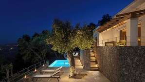 Un espace piscine extérieur moderne, agrémenté d’un mur en pierre, d’une terrasse en bois et de chaises longues.