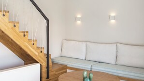 Un intérieur moderne avec un escalier en bois, une table de salle à manger ronde, un canapé et deux lampes suspendues.